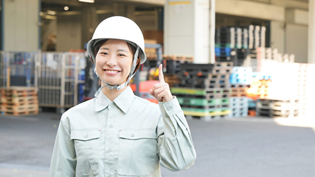 ヘルメットを被って倉庫の前に立つ女性