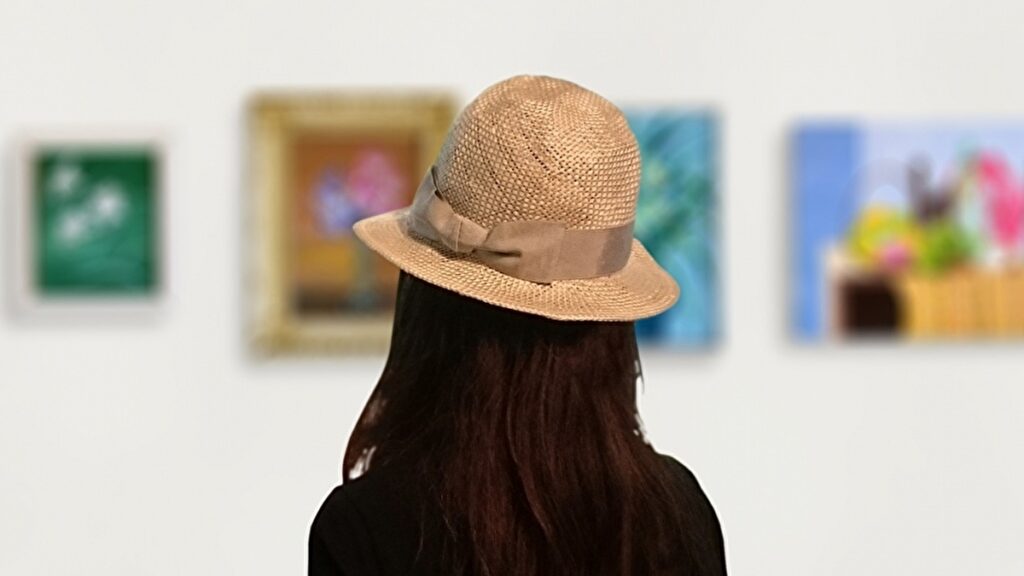 絵画を鑑賞する麦わら帽子をかぶった女性の後ろ姿