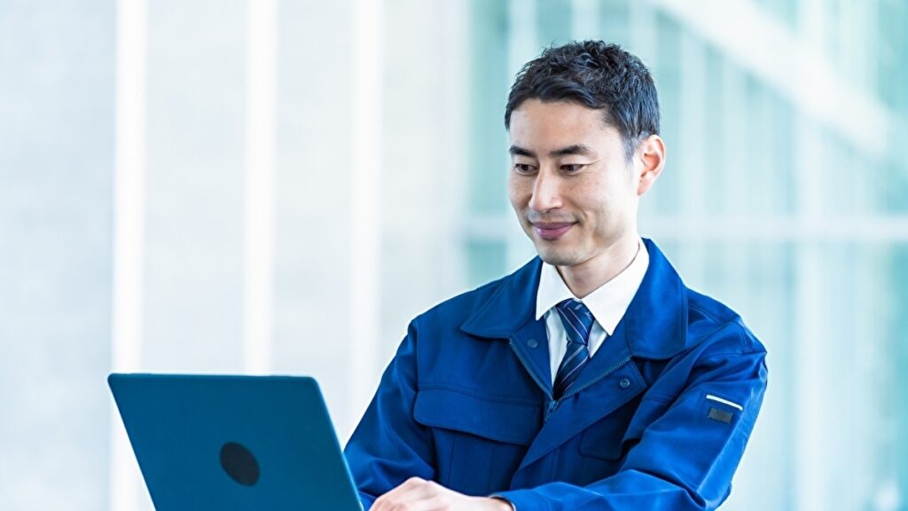 青い作業着でパソコンを操作する男性