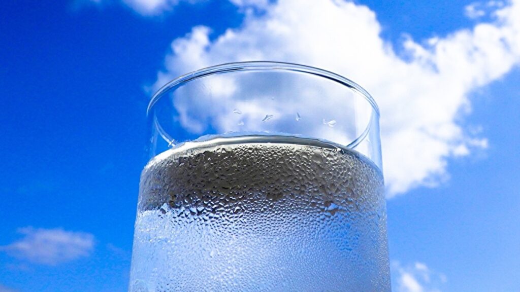 青空を背景に置かれた水の入ったグラス