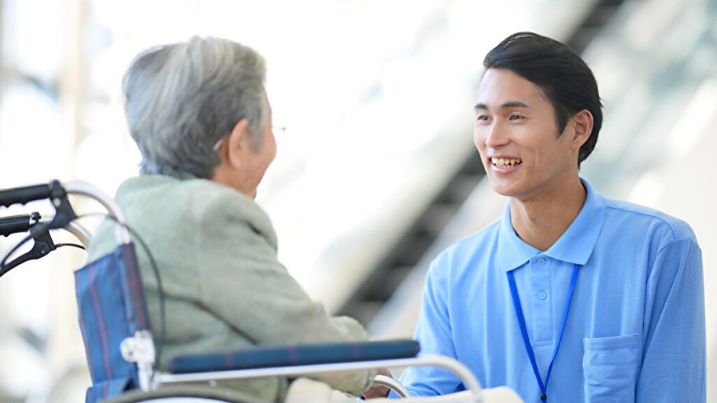 車椅子のお年寄りと話す青いポロシャツを着た男性介護士