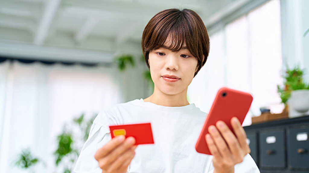 赤いスマートフォンとクレジットカードを見つめる女性