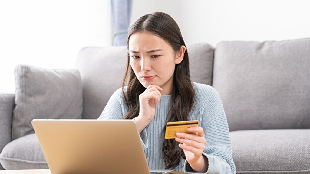 パソコンの前でクレジットカードを持って考える女性